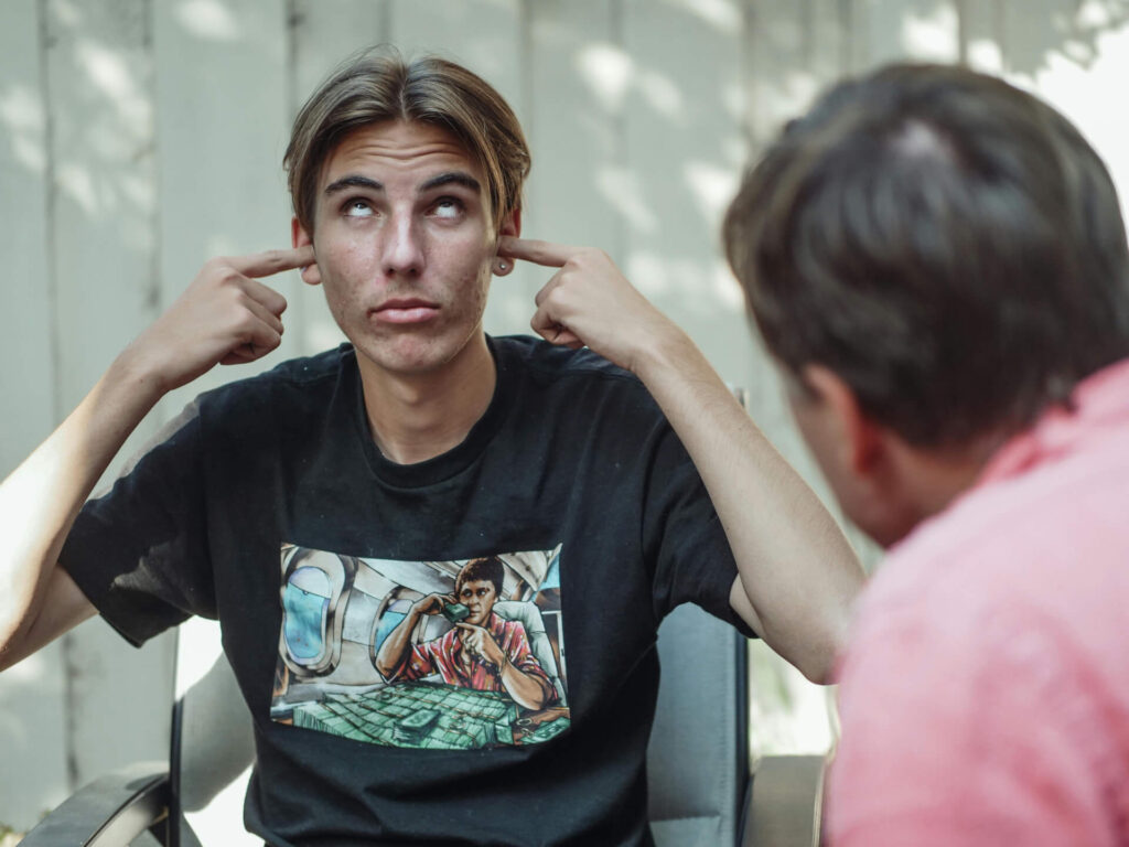 A teen covering his ear while his father is talking